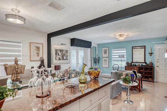 kitchen featuring beam ceiling, dark stone countertops, white cabinetry, and light tile patterned flooring