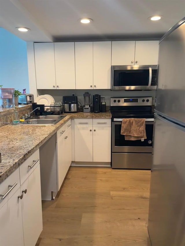 kitchen with sink, light wood-type flooring, light stone counters, white cabinetry, and stainless steel appliances