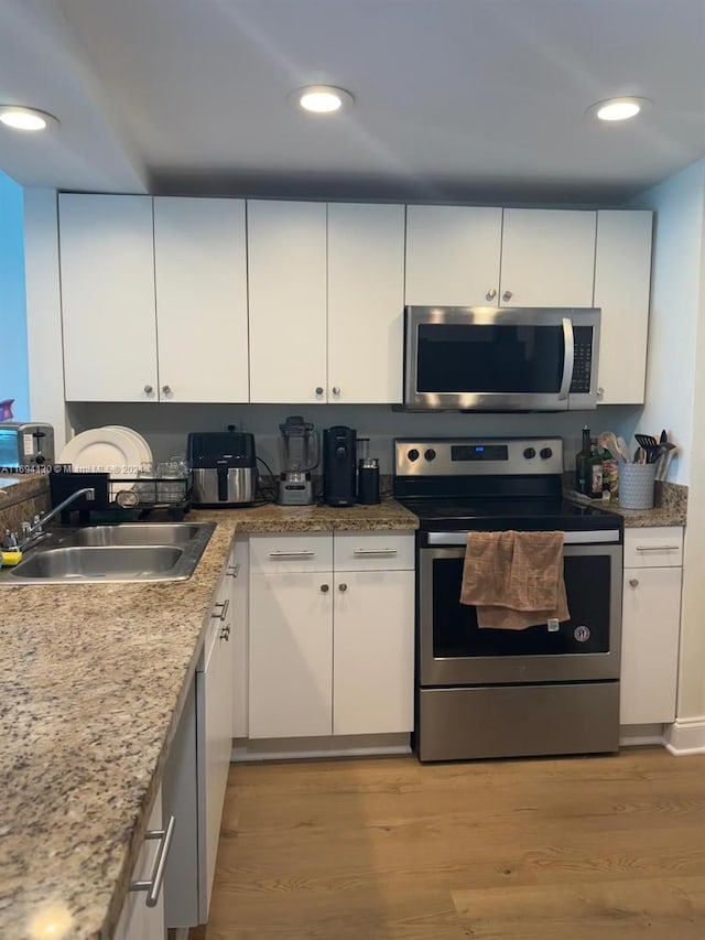 kitchen with appliances with stainless steel finishes, light hardwood / wood-style floors, white cabinetry, and sink