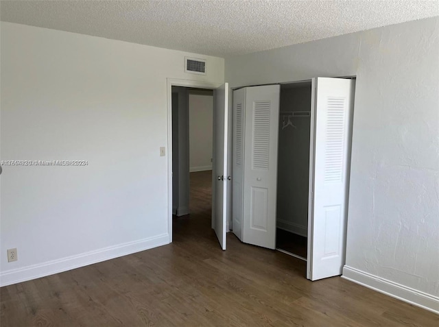 unfurnished bedroom with a textured ceiling, dark hardwood / wood-style flooring, and a closet