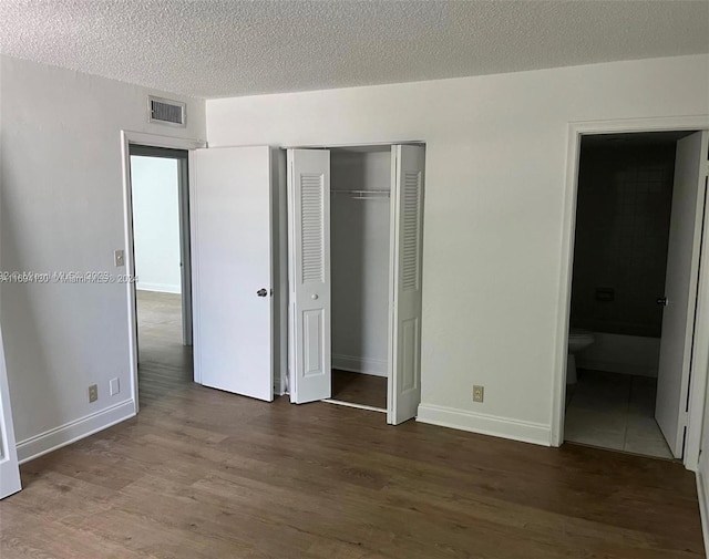 unfurnished bedroom featuring ensuite bath, a closet, dark hardwood / wood-style flooring, and a textured ceiling