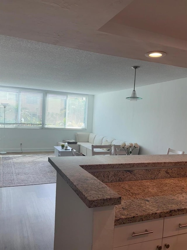 kitchen with hanging light fixtures, dark stone counters, a textured ceiling, white cabinets, and hardwood / wood-style flooring