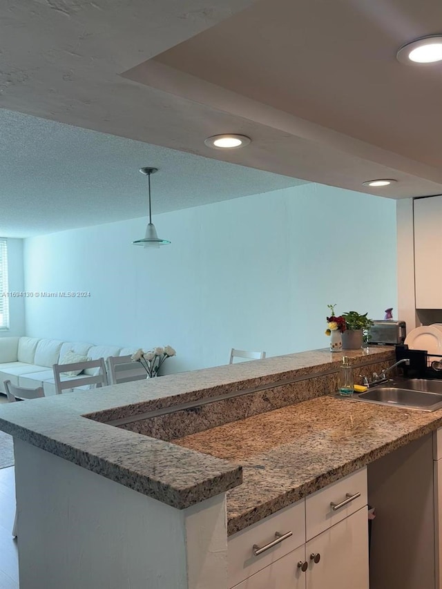 kitchen with pendant lighting, white cabinets, sink, dark stone countertops, and kitchen peninsula