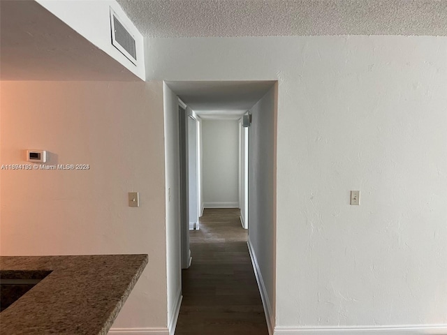 hallway with a textured ceiling and dark hardwood / wood-style floors