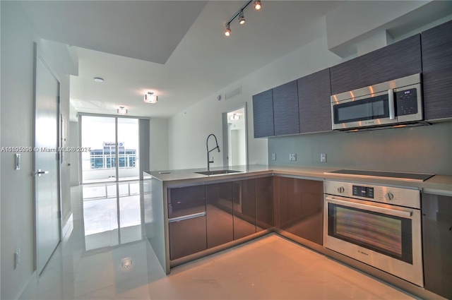 kitchen with kitchen peninsula, appliances with stainless steel finishes, floor to ceiling windows, and sink