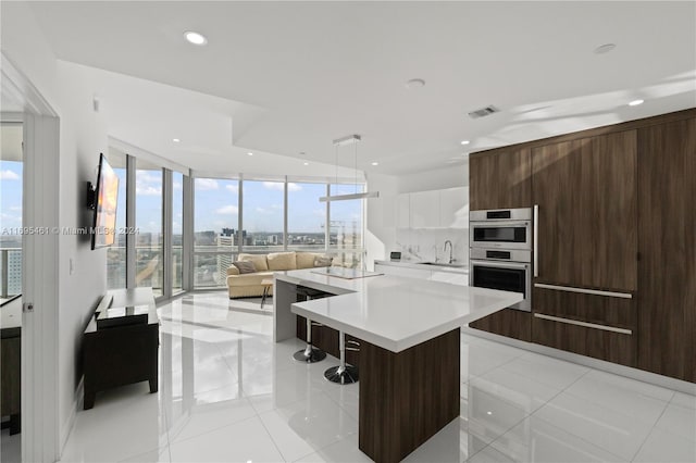 kitchen with a center island, floor to ceiling windows, a kitchen breakfast bar, double oven, and white cabinetry