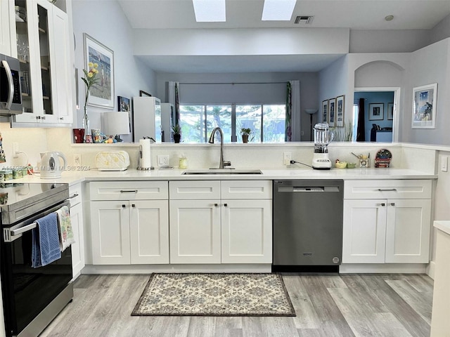 kitchen featuring white cabinets, sink, a skylight, light hardwood / wood-style floors, and stainless steel appliances