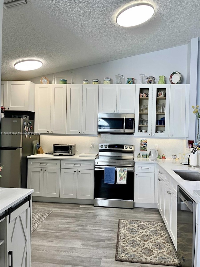 kitchen with white cabinetry, sink, stainless steel appliances, and vaulted ceiling