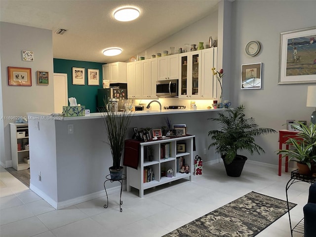 kitchen featuring lofted ceiling, white cabinetry, kitchen peninsula, and appliances with stainless steel finishes