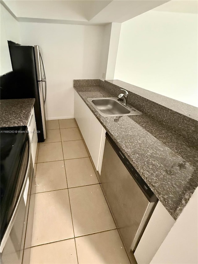 kitchen featuring sink, dark stone countertops, appliances with stainless steel finishes, light tile patterned flooring, and white cabinetry