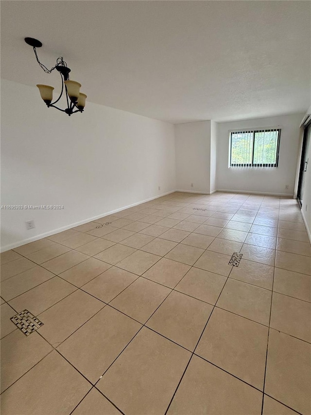 tiled spare room featuring an inviting chandelier