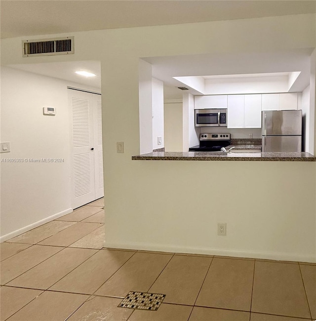 kitchen with kitchen peninsula, stainless steel appliances, light tile patterned floors, dark stone countertops, and white cabinetry