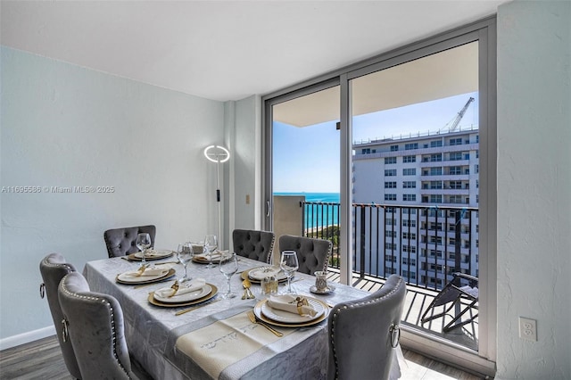 dining space featuring hardwood / wood-style floors, a wall of windows, and a water view