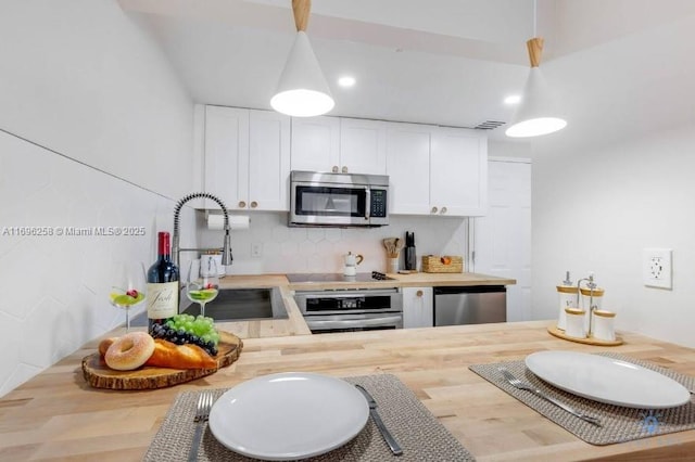 kitchen with white cabinetry, butcher block counters, stainless steel appliances, sink, and hanging light fixtures