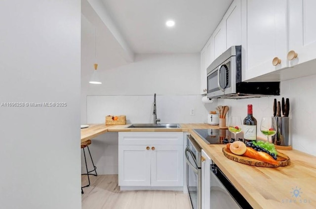 kitchen with white cabinetry, stainless steel appliances, sink, backsplash, and butcher block countertops