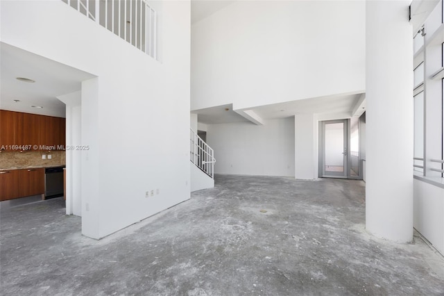 unfurnished living room with unfinished concrete flooring, a high ceiling, and stairs