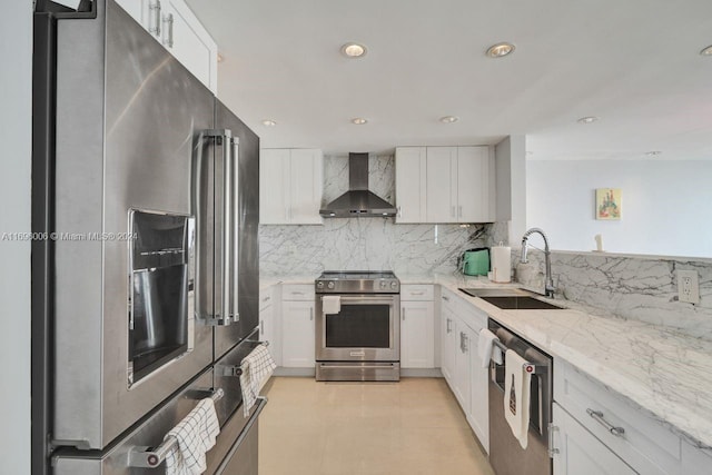 kitchen with sink, wall chimney exhaust hood, light stone counters, white cabinets, and appliances with stainless steel finishes