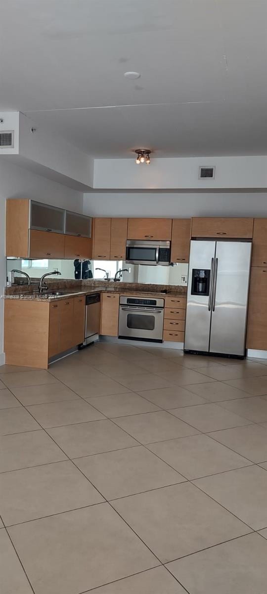 kitchen with light tile patterned floors, appliances with stainless steel finishes, and dark stone counters