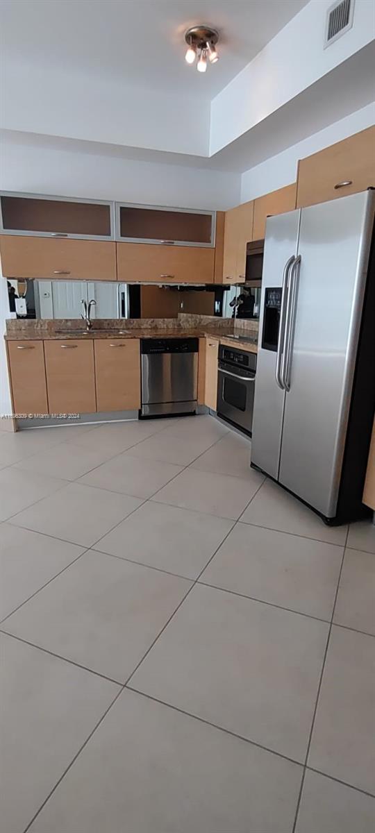 kitchen featuring appliances with stainless steel finishes, light tile patterned floors, light brown cabinetry, and sink