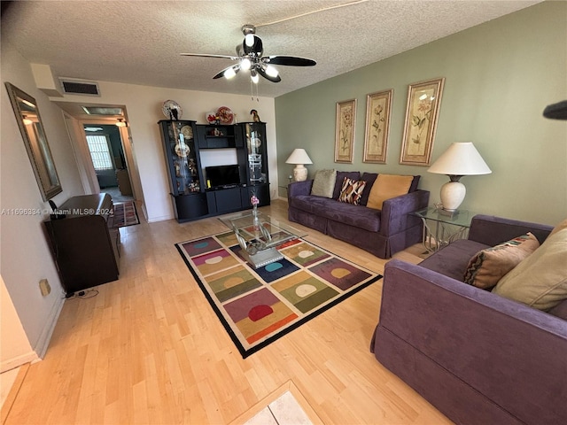 living room featuring ceiling fan, light hardwood / wood-style flooring, and a textured ceiling