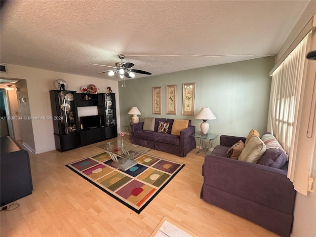 living room featuring ceiling fan, light hardwood / wood-style floors, and a textured ceiling