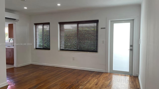 empty room with a wall mounted air conditioner, dark hardwood / wood-style flooring, a healthy amount of sunlight, and sink