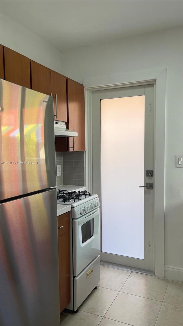 kitchen featuring light tile patterned floors, white range with gas stovetop, stainless steel refrigerator, and tasteful backsplash