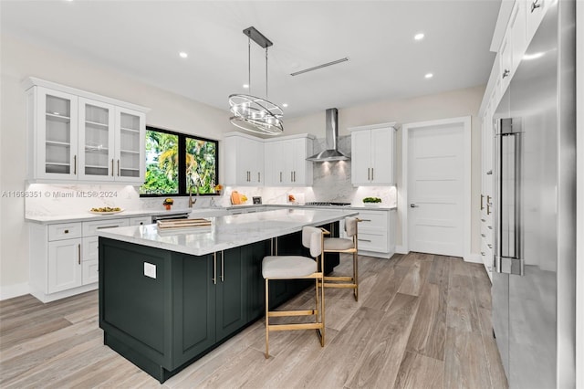 kitchen featuring a spacious island, wall chimney range hood, light hardwood / wood-style flooring, decorative light fixtures, and white cabinetry