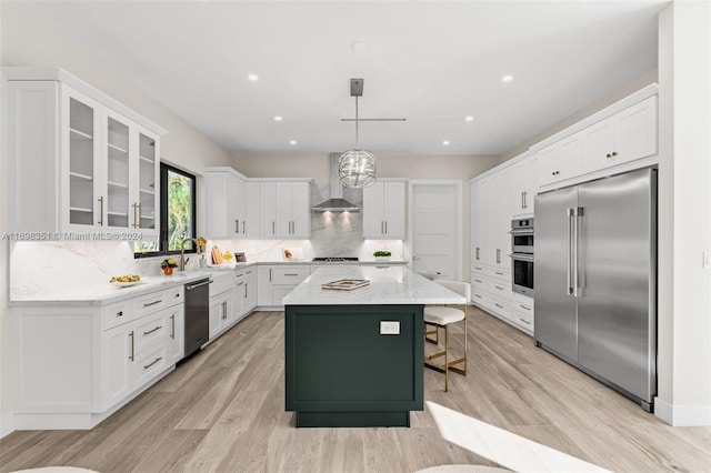 kitchen featuring appliances with stainless steel finishes, wall chimney exhaust hood, pendant lighting, a center island, and light hardwood / wood-style floors