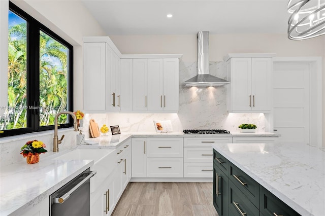 kitchen featuring pendant lighting, wall chimney range hood, light stone countertops, appliances with stainless steel finishes, and white cabinetry