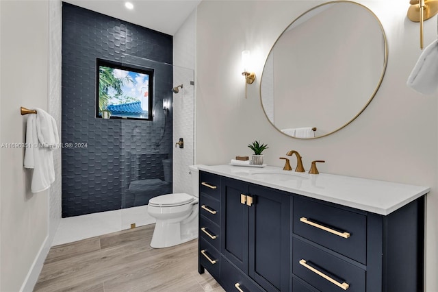 bathroom with hardwood / wood-style floors, vanity, toilet, and a tile shower