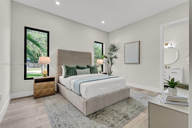 bedroom with light hardwood / wood-style floors, connected bathroom, and multiple windows