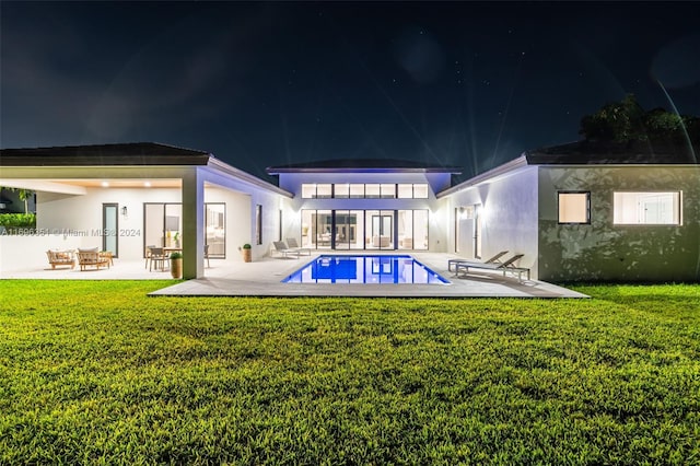 back house at night featuring a patio area and a yard