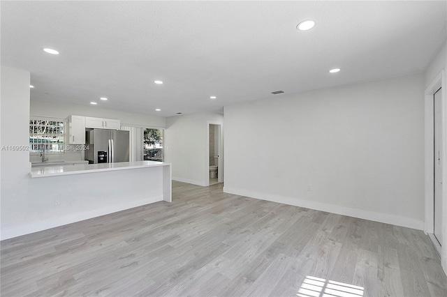 unfurnished living room featuring a wealth of natural light, sink, and light wood-type flooring