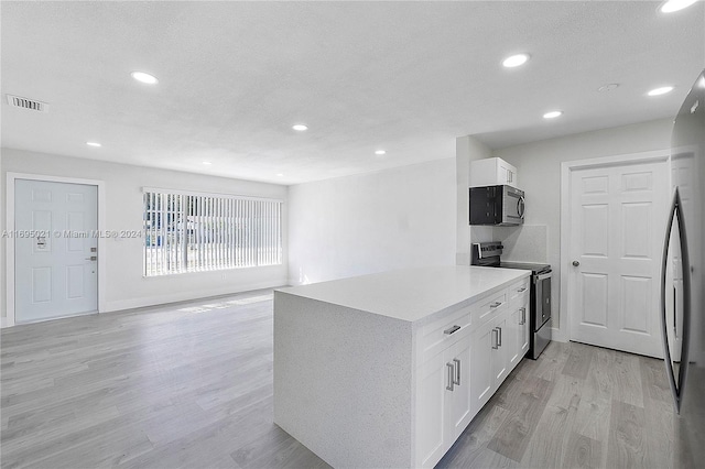 kitchen with white cabinets, light wood-type flooring, a textured ceiling, and appliances with stainless steel finishes