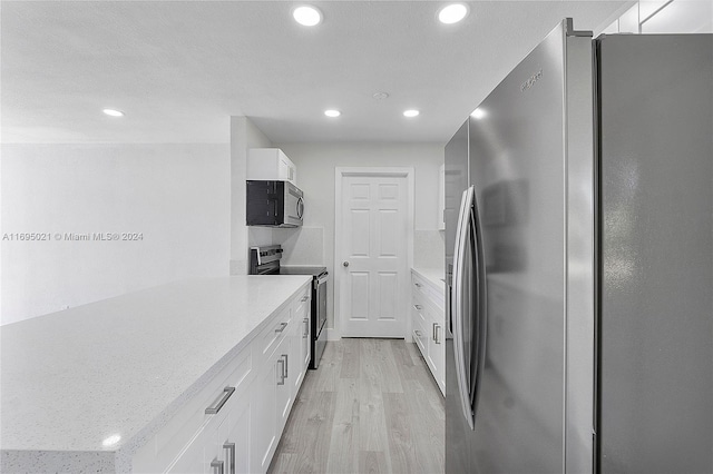 kitchen with white cabinets, light wood-type flooring, and appliances with stainless steel finishes