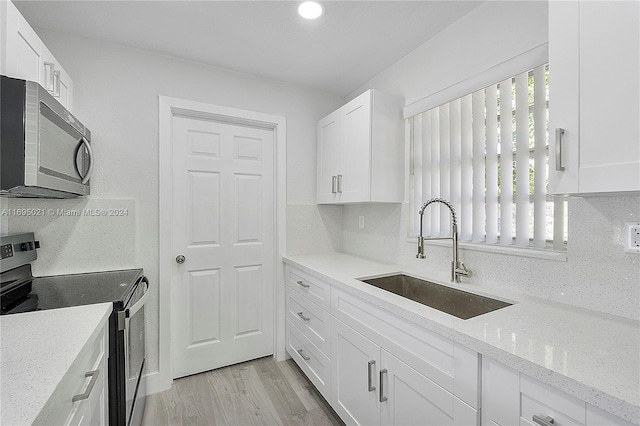 kitchen featuring light stone countertops, appliances with stainless steel finishes, sink, white cabinets, and light hardwood / wood-style floors