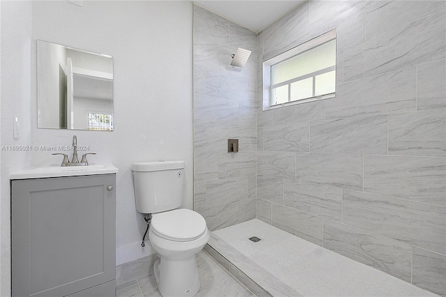 bathroom featuring a tile shower, vanity, toilet, and a healthy amount of sunlight