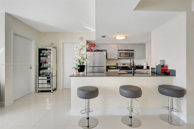 kitchen with kitchen peninsula, a breakfast bar, gray cabinetry, and appliances with stainless steel finishes