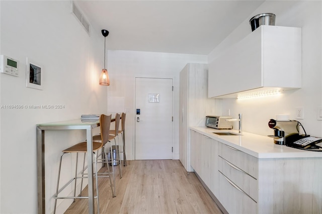 6080 Collins Ave Unit 102, Miami Beach, FL 33140 - kitchen with modern cabinets, light wood finished floors, light countertops, white cabinets, and pendant lighting