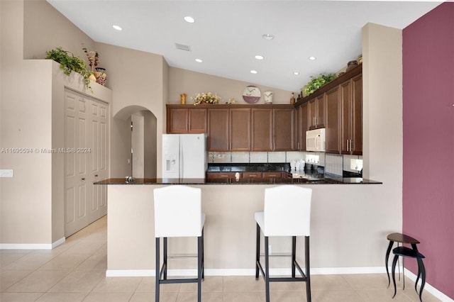 kitchen featuring a kitchen breakfast bar, white appliances, kitchen peninsula, and vaulted ceiling