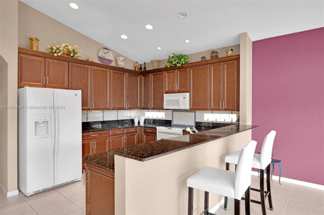 kitchen with kitchen peninsula, dark stone counters, white appliances, light tile patterned floors, and lofted ceiling