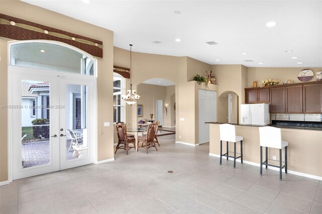 kitchen featuring french doors, pendant lighting, light tile patterned floors, white fridge with ice dispenser, and a breakfast bar area