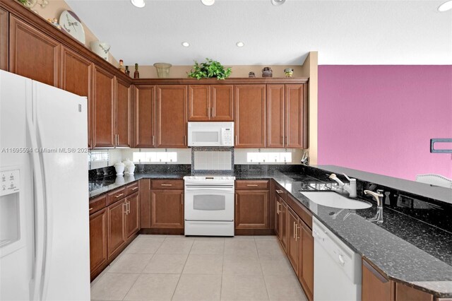 kitchen with dark stone countertops, sink, light tile patterned floors, and white appliances