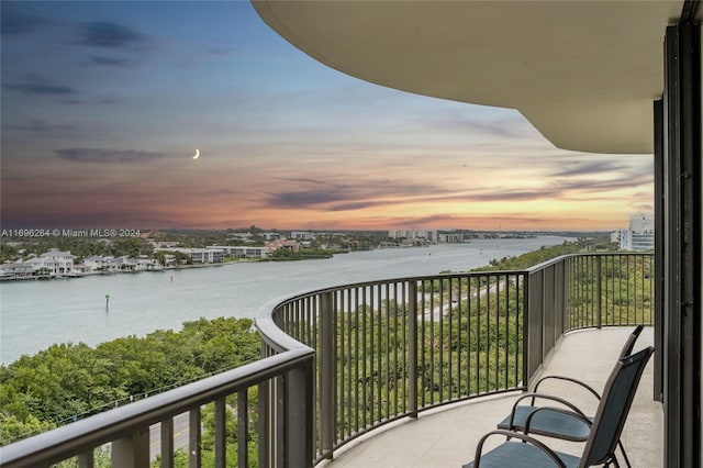 balcony at dusk featuring a water view