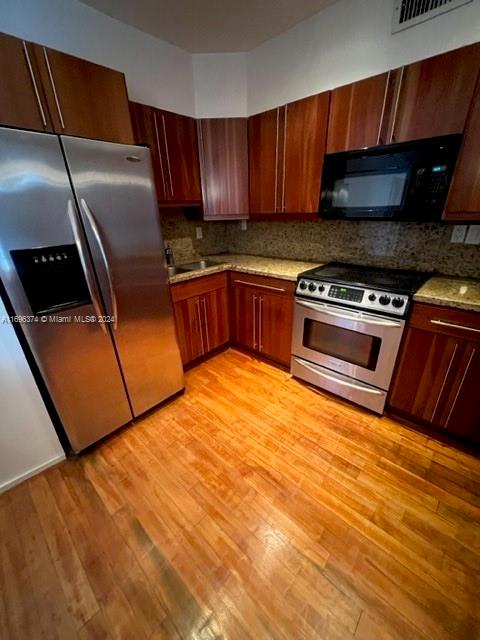 kitchen featuring sink, tasteful backsplash, light stone counters, appliances with stainless steel finishes, and light wood-type flooring