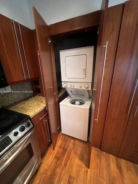 laundry area with light wood-type flooring and stacked washer / dryer