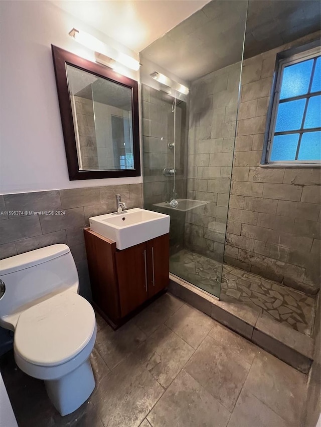 bathroom with tiled shower, vanity, tile walls, and toilet