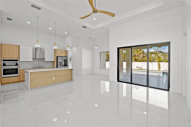 kitchen featuring white cabinetry, ceiling fan, stainless steel appliances, wall chimney range hood, and a tray ceiling