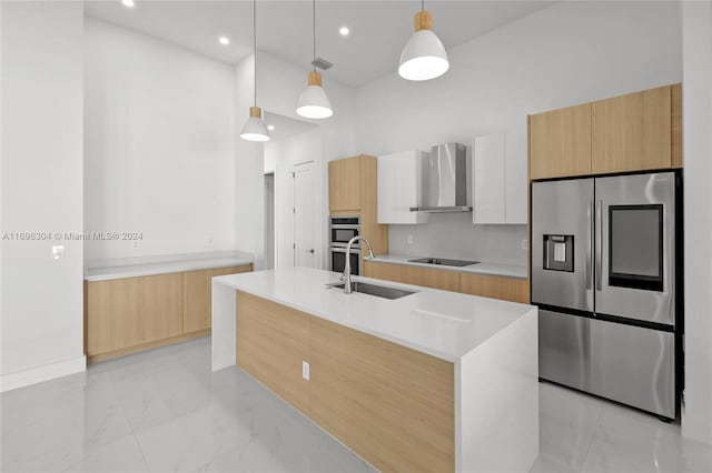 kitchen featuring appliances with stainless steel finishes, wall chimney exhaust hood, pendant lighting, a center island with sink, and white cabinets